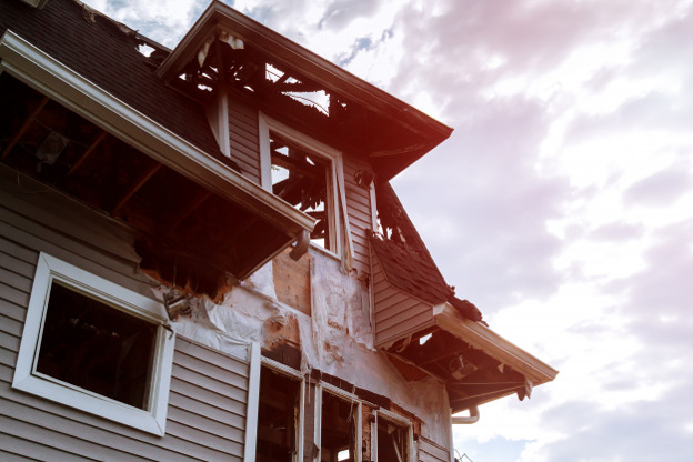 Fire-damaged home with severe roof and exterior structural damage.