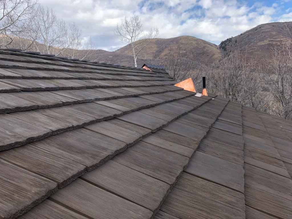Close-up of synthetic cedar shake roofing with a mountain landscape in the background.