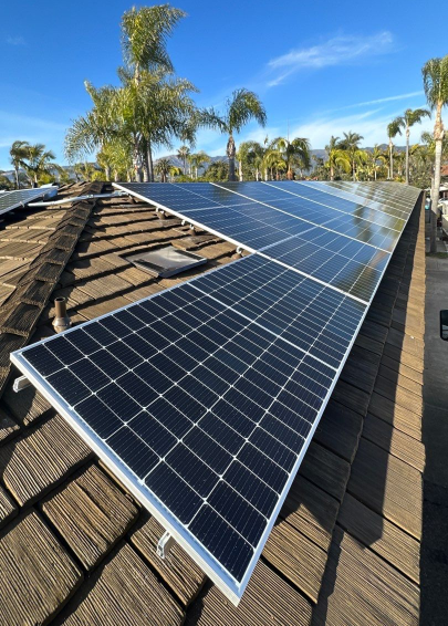 Solar panels installed on a cedar shake roof surrounded by palm trees.