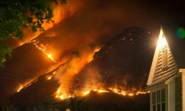 Wildfire burning near homes, highlighting the threat of fire-prone environments.