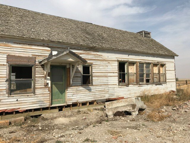 An old, crumbling schoolhouse with peeling paint and sagging walls.