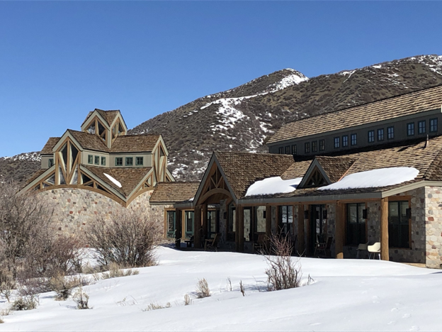 A house in the middle of the mountains with snow on the roof. 