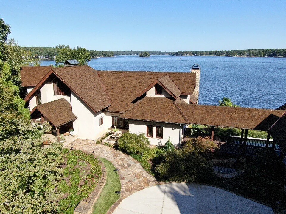 A two story house with brown synthetic roofing materials near a lake.