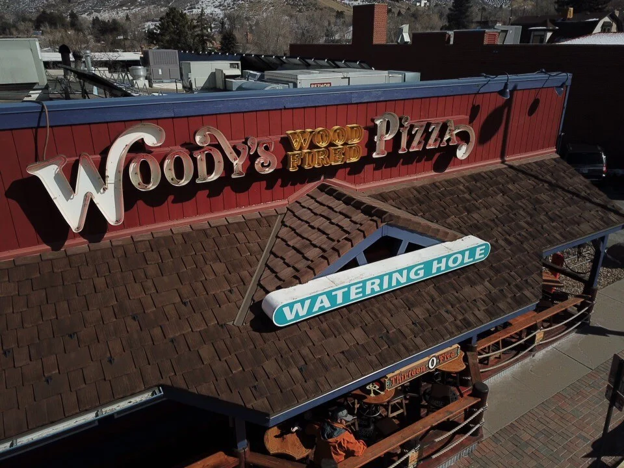Woody’s Wood Fired Pizza in Golden, Colorado with red paneled siding and CEDUR Live Oak roofing over a porch seating area.