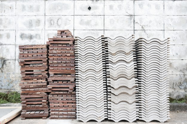 Stacks of newly made concrete roof tiles arranged against an outdoor wall.